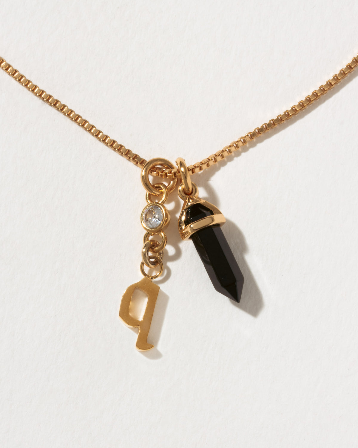 Necklace with gold chain, black crystal pendant, and gold 'Q' charm on a white background
