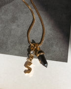 Gold necklace with a letter 's' and black crystal pendant on a gray and white background