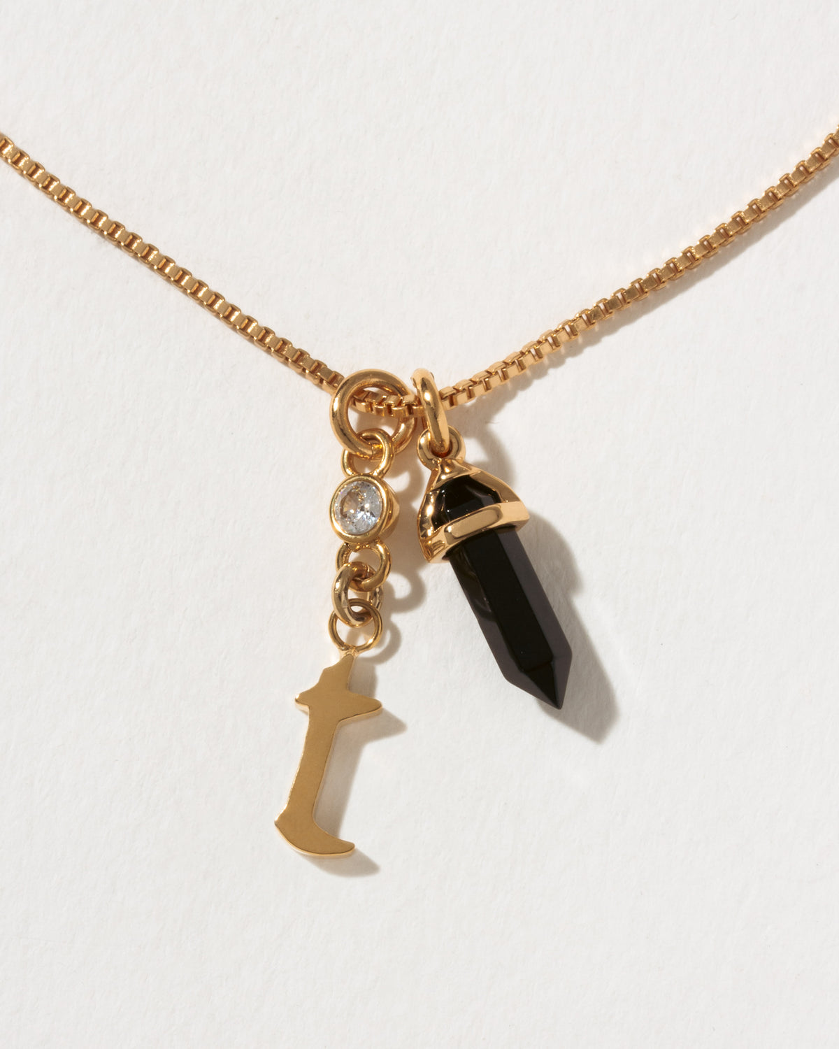 Necklace with gold chain, black crystal pendant, and gold letter 't' charm on a white background