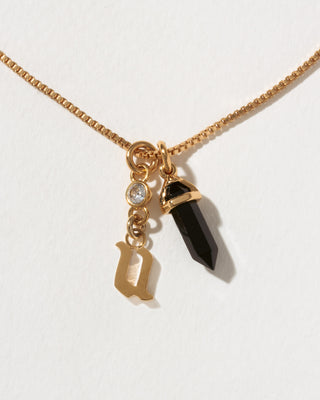 Necklace with gold chain, black crystal pendant, and gold letter 'u' charm on a white background