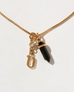 Necklace with gold chain, black crystal pendant, and gold letter 'v' charm on a white background