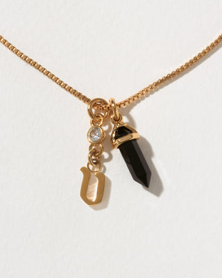 Necklace with gold chain, black crystal pendant, and gold letter 'v' charm on a white background