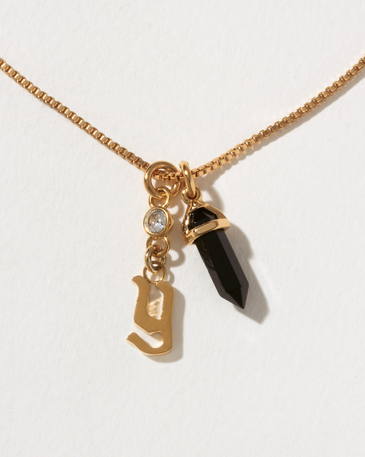 Necklace with gold charm, black crystal, and letter 'y' on a white background