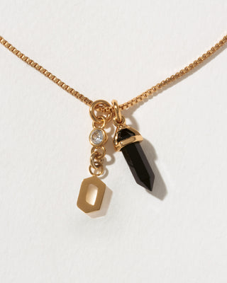 Necklace with gold chain, black crystal pendant, and gold letter 'o' charm on a white background