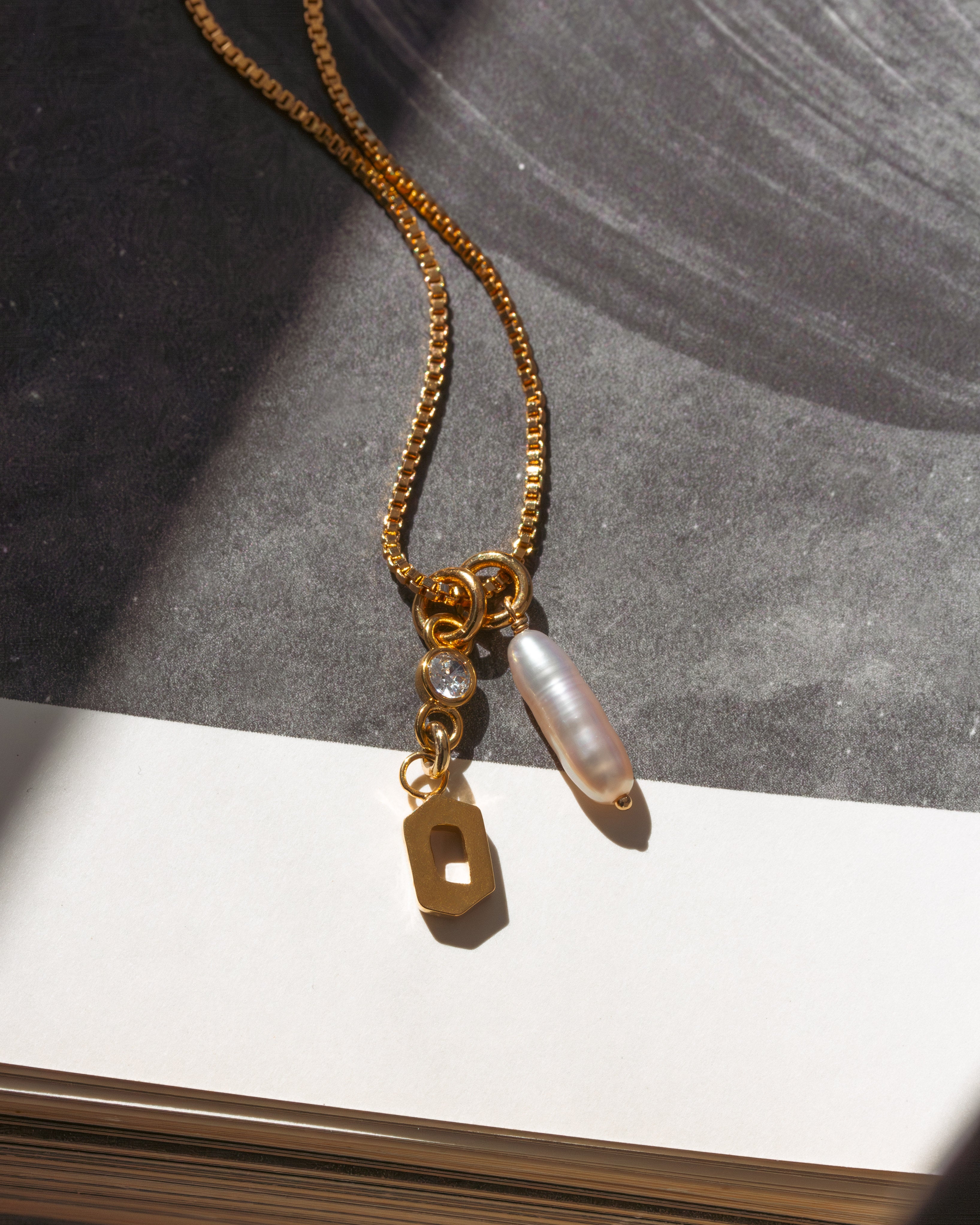 Gold necklace with O charm, a sparkling CZ accent, and freshwater stick pearl on a box chain.