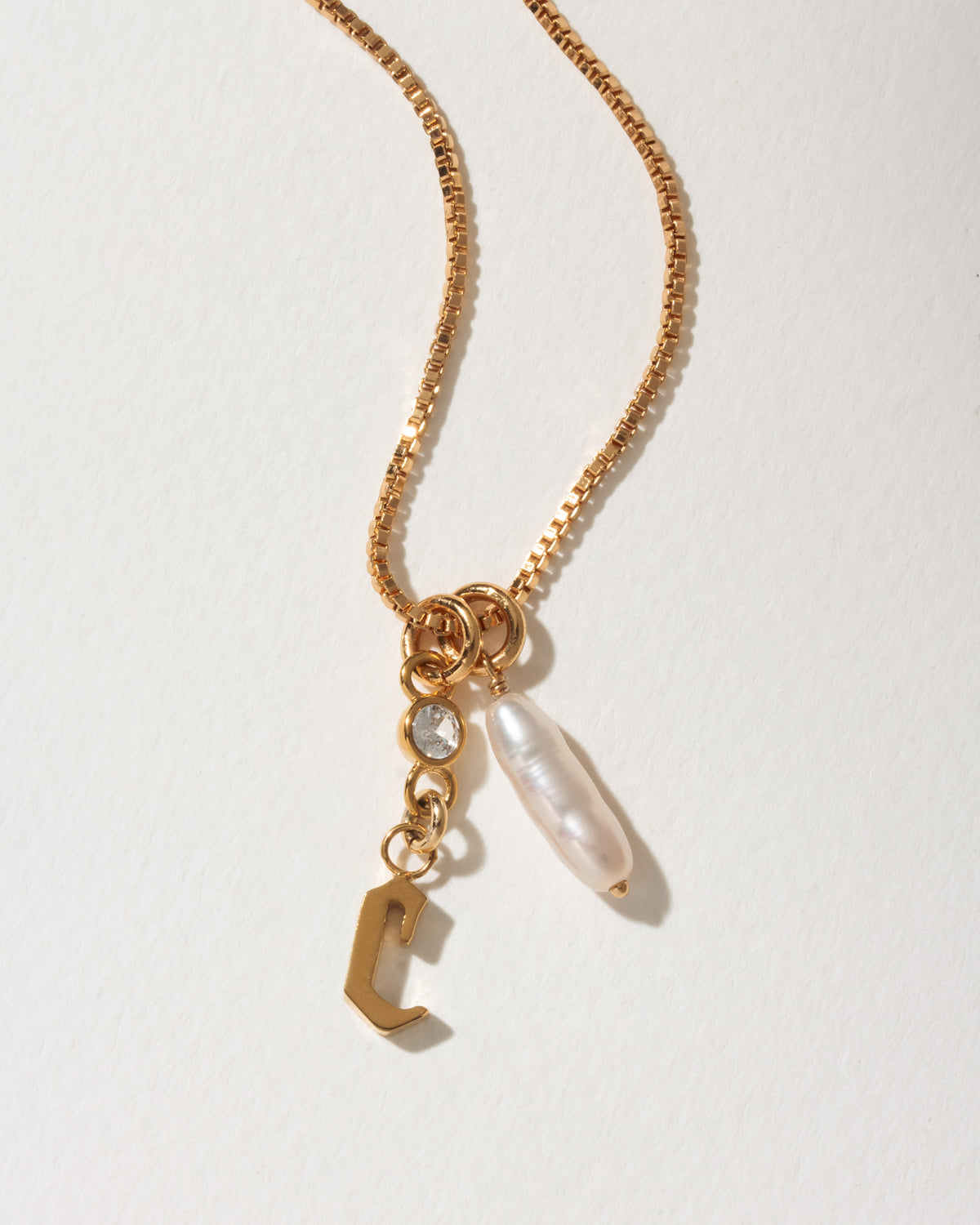 Gold necklace with C charm, clear crystal, and an oblong white pearl.