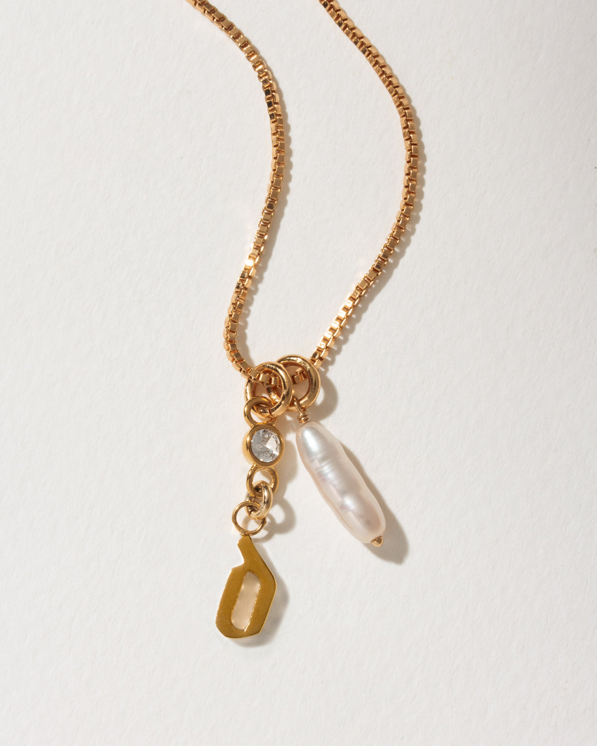Gold box chain necklace with a baroque pearl, clear gemstone, and a gold letter D initial pendant.