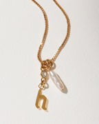 Gold box chain necklace with a clear crystal, a baroque pearl, and a lowercase letter 'h' pendant.