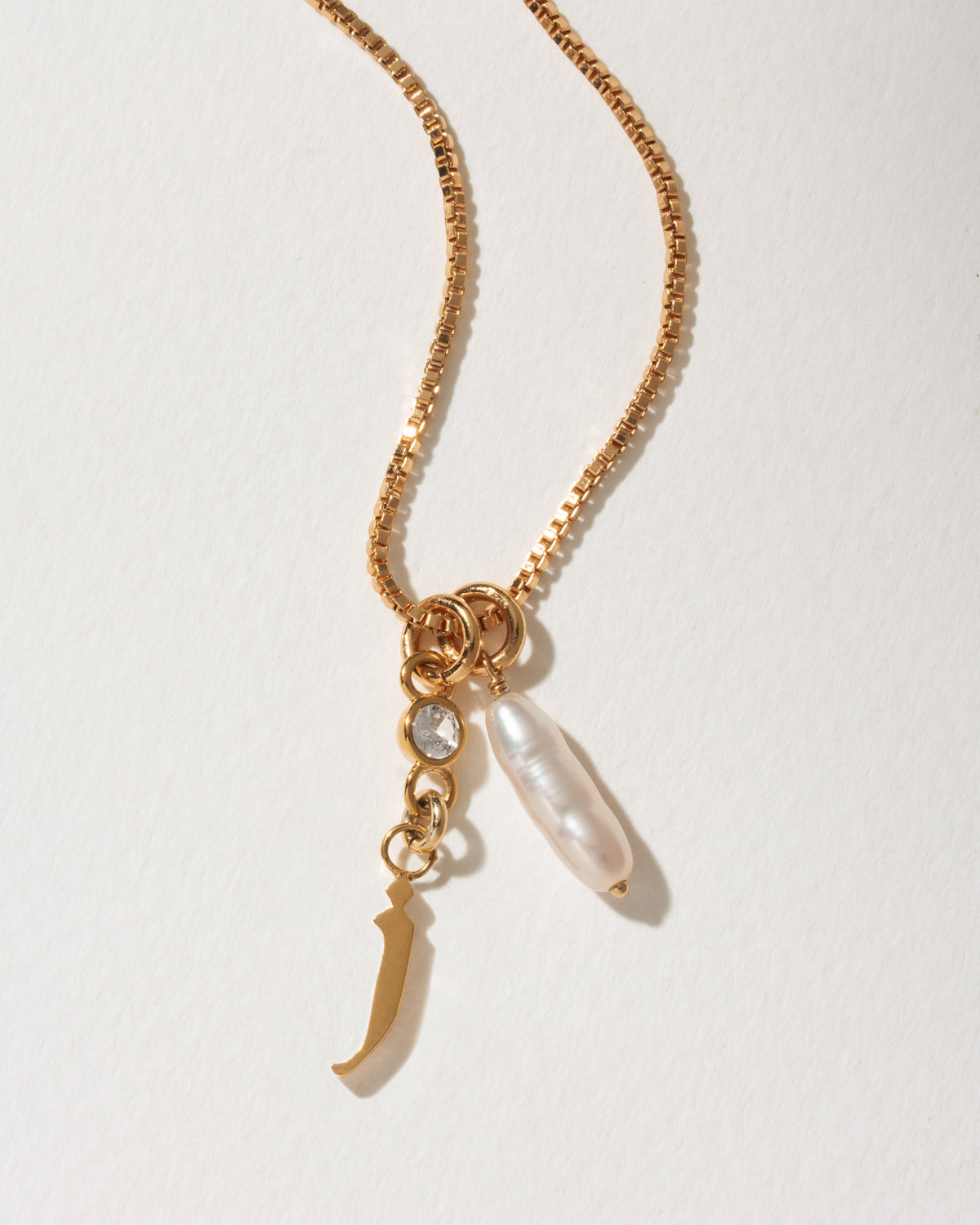 Gold necklace with J charm, clear crystal, and baroque pearl.