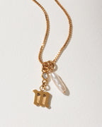 Gold box chain necklace with a stylized lowercase letter M charm, a small crystal, and an pearl.