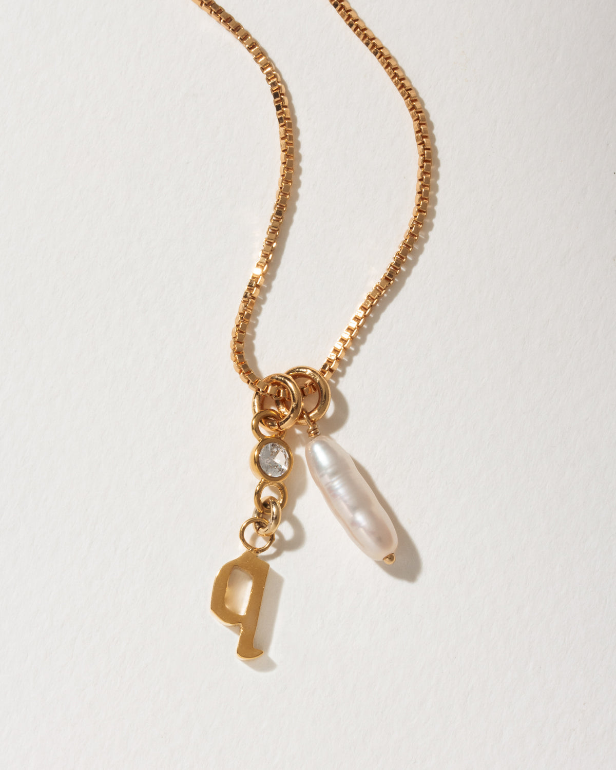 Gold box chain necklace with a lowercase q initial charm, clear crystal, and a long pearl drop.