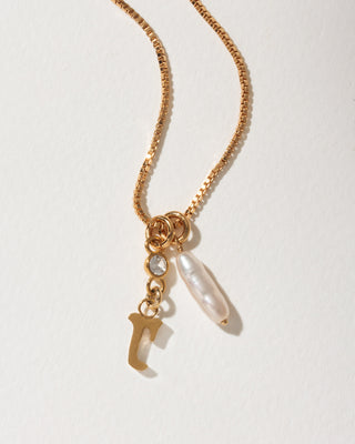 Gold box chain necklace featuring a dangling letter J charm, a small round crystal, and an elongated white pearl.