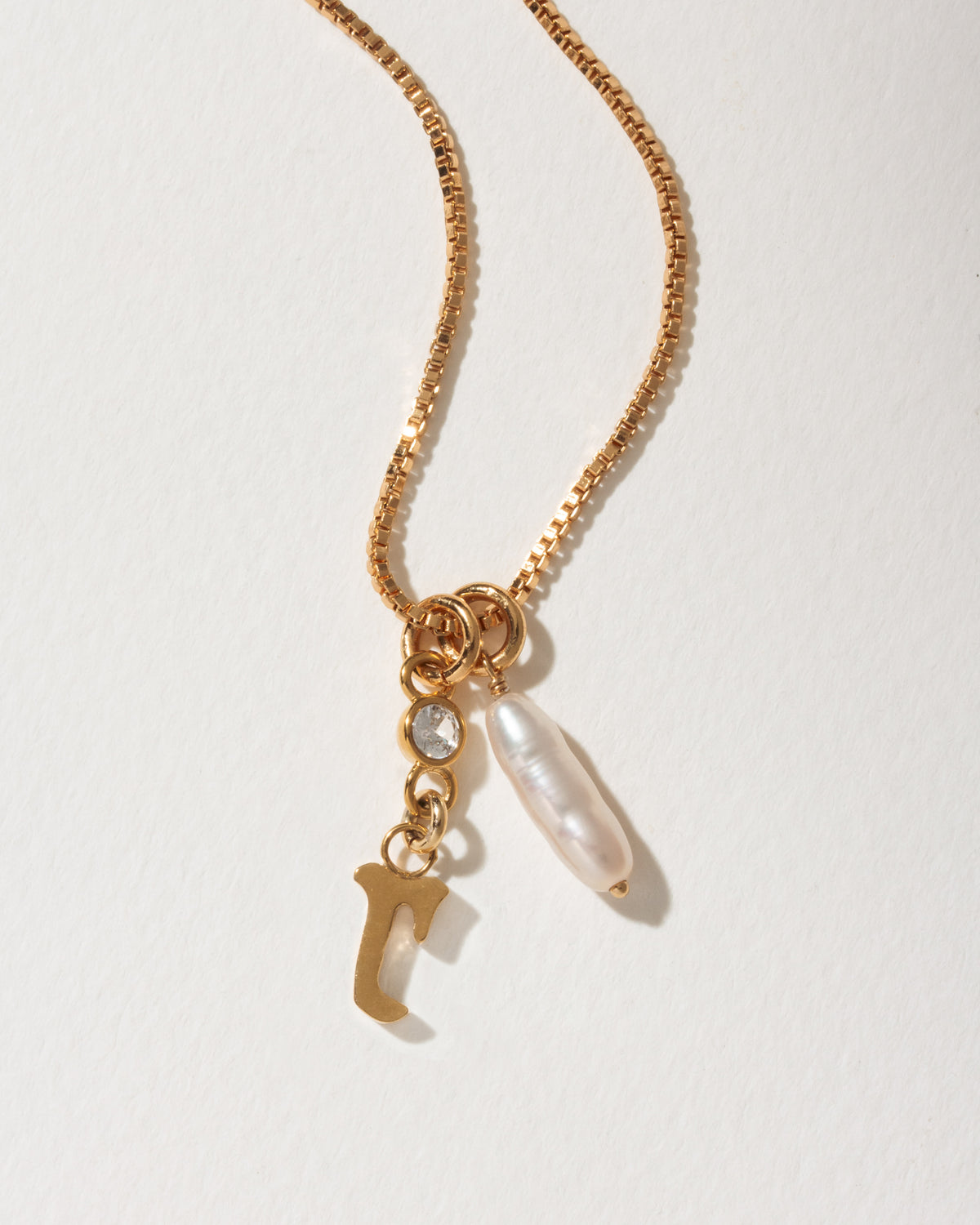Gold box chain necklace with a dangling letter J charm, a small crystal, and an long pearl.