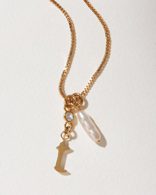 Gold box chain necklace featuring a capital letter I charm, a small clear crystal, and a white baroque pearl.