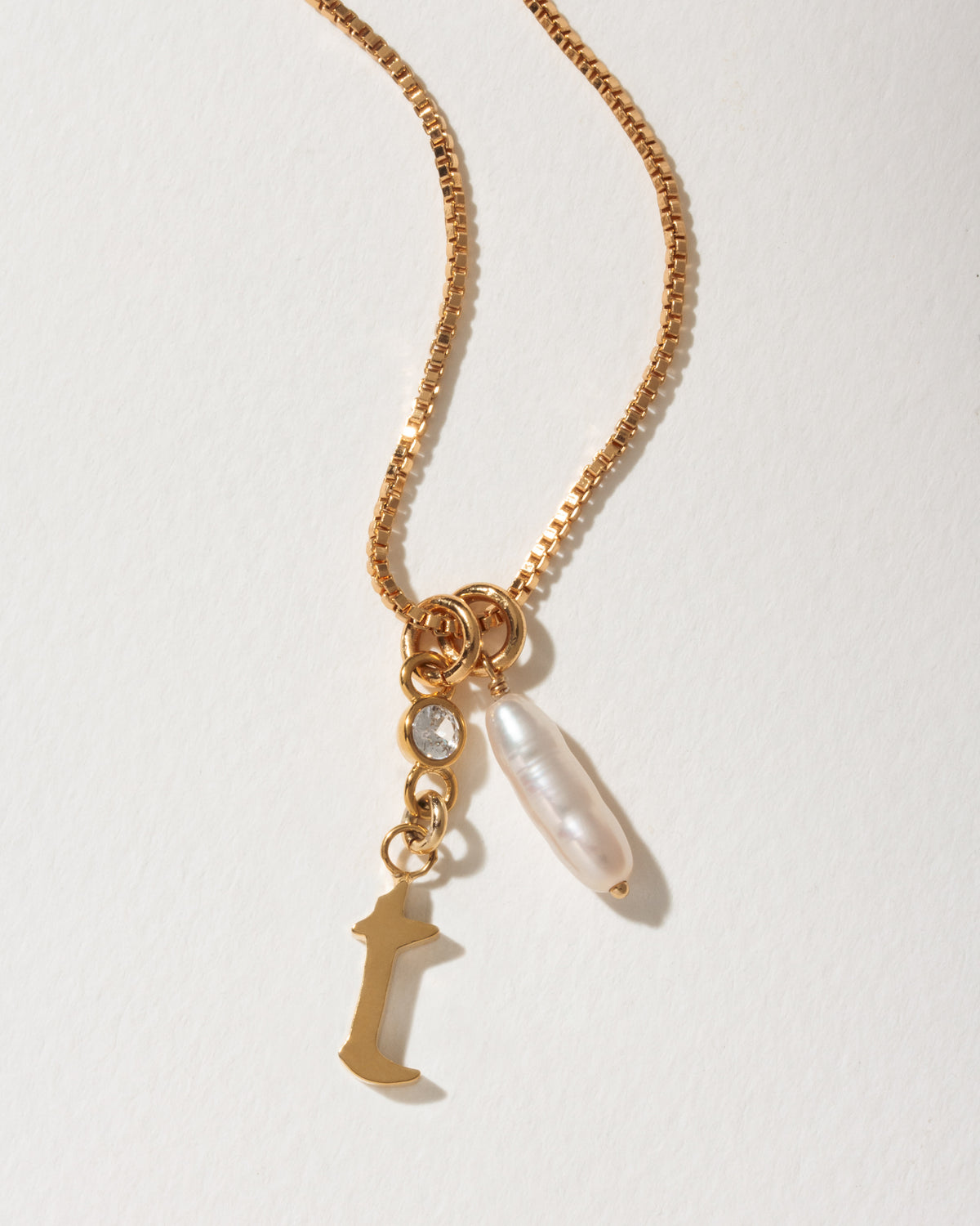 Gold box chain necklace with a capital letter I charm, a small clear crystal, and a baroque pearl.