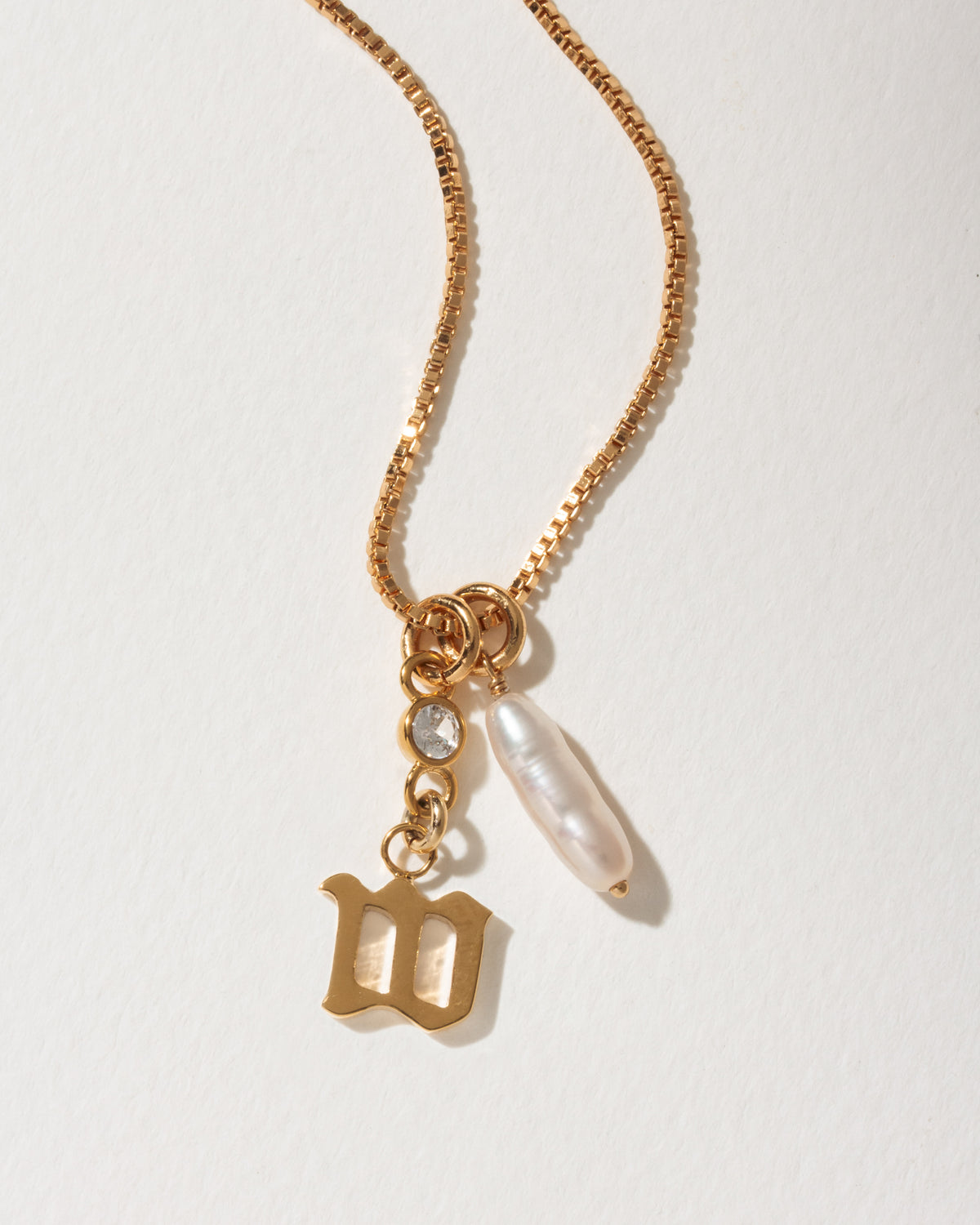 Gold necklace with an Old English letter M pendant, a baroque pearl, and clear crystal.