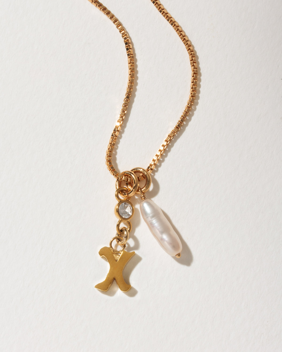 Gold box chain necklace with a letter X initial pendant, a small clear crystal, and a baroque pearl.