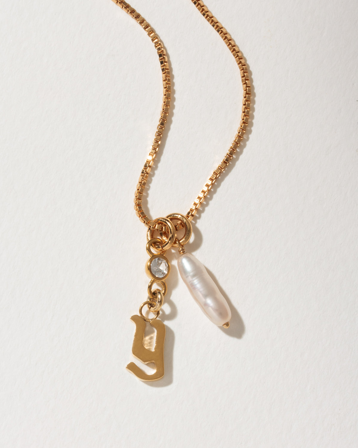 Gold box chain necklace with a lowercase gothic letter G charm, an long pearl, and a clear crystal.