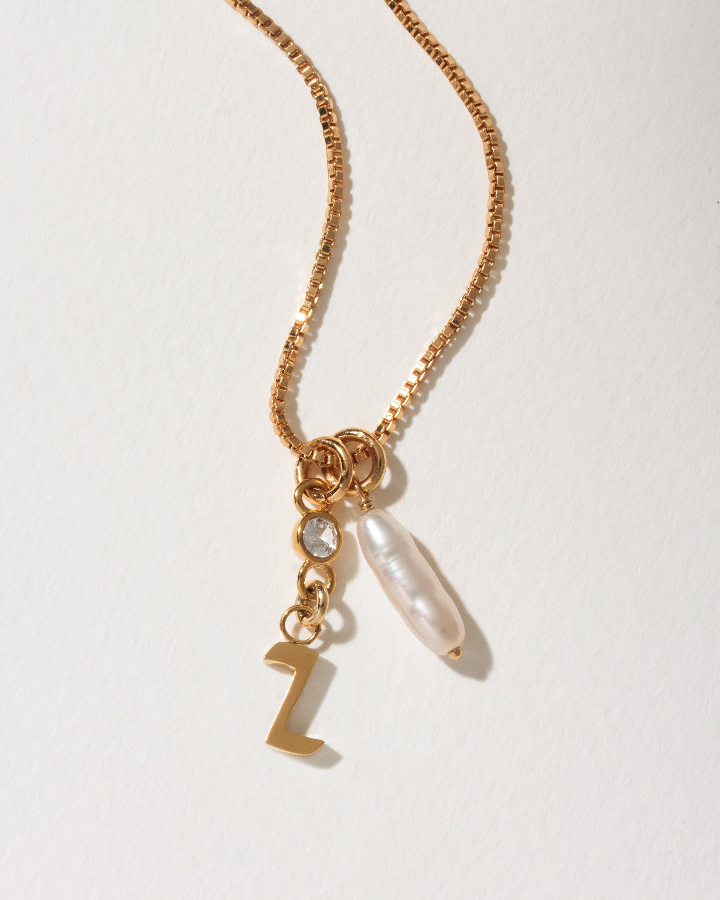 Gold box chain necklace with a "Z" initial charm, a small clear crystal, and an long pearl pendant.