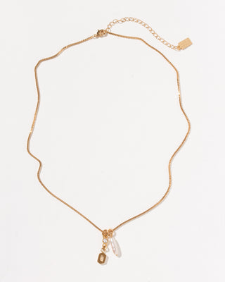 Gold box chain necklace with a small crystal, a white pearl charm, and a gold letter O initial pendant.