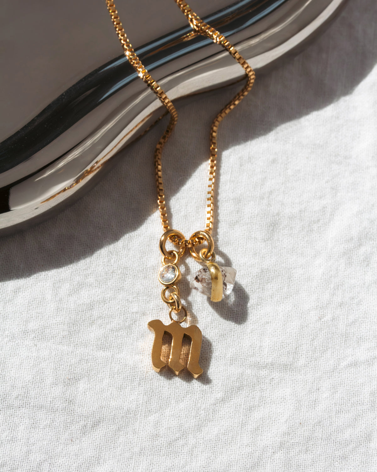 Gold necklace with lowercase m charm, a clear CZ accent, and Herkimer quartz.