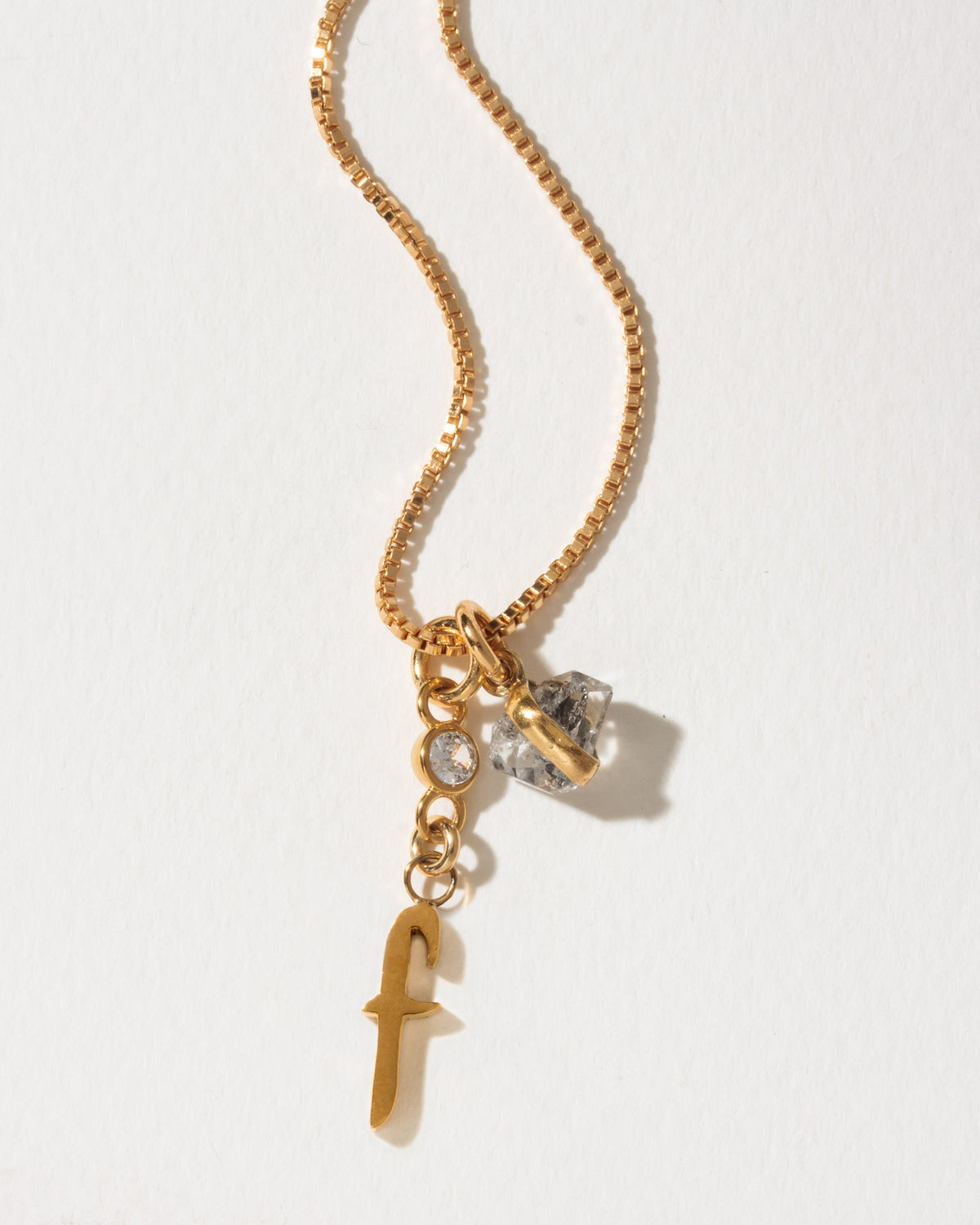 Gold necklace with lowercase f charm alongside crystal and Herkimer quartz.
