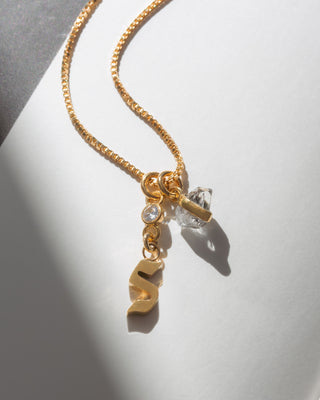 Gold box chain necklace featuring a gold initial S charm, a small round crystal, and a herkimer quartz quartz pendant.