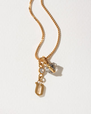 Gold box chain necklace featuring an initial U pendant, a small clear crystal, and a raw Herkimer diamond-style charm.