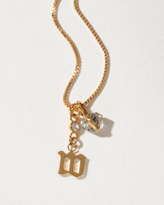 Gold box chain necklace featuring a round clear stone, a herkimer quartz charm, and a gothic-style letter M initial pendant.