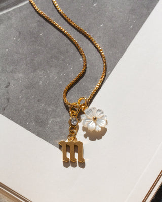 Gold necklace with a letter 'm' and flower pendant on a gray and white background