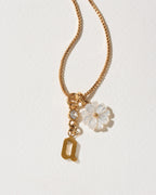 Gold necklace with a flower charm and letter 'a' on a light background