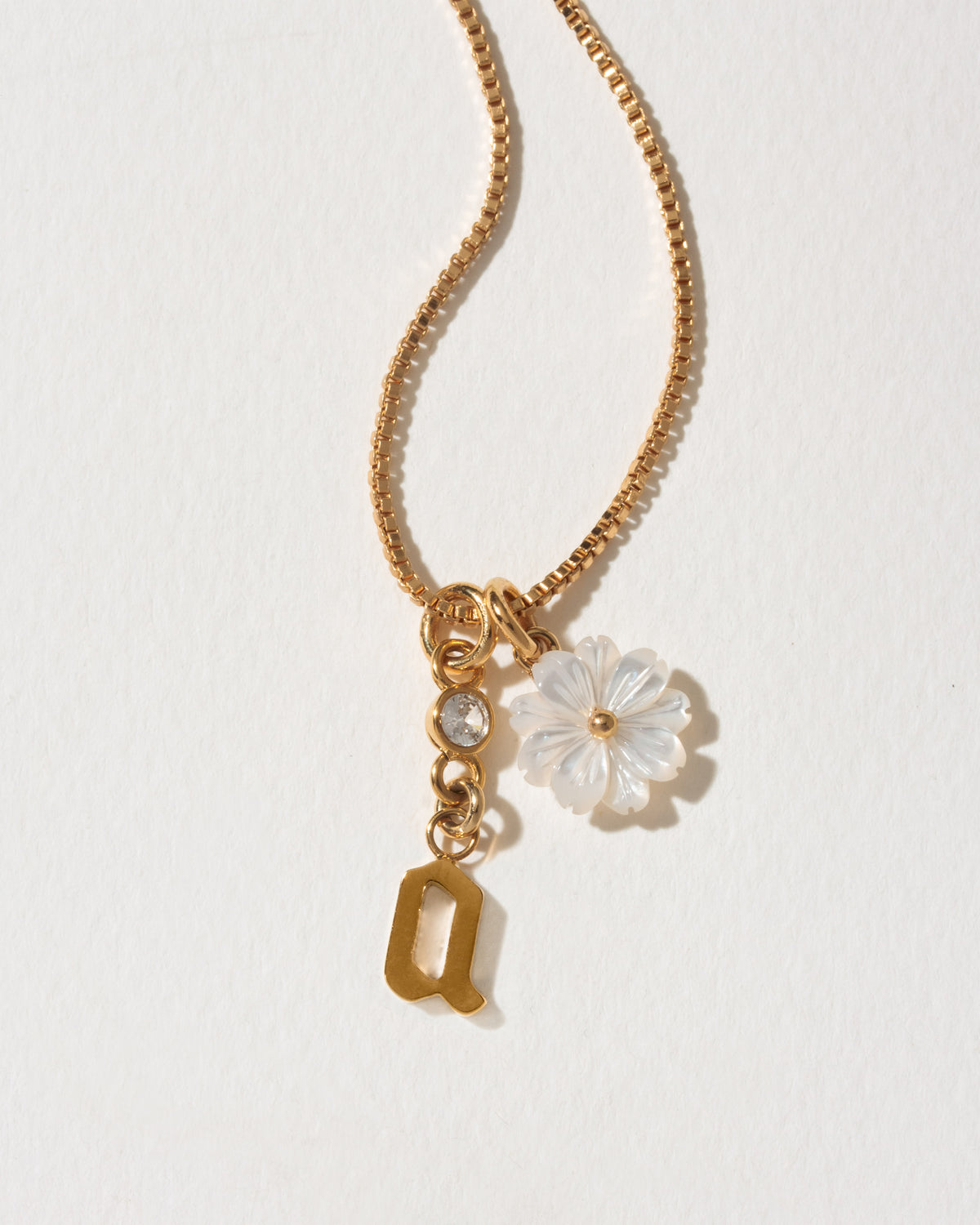Gold necklace with a flower charm and letter 'a' on a light background