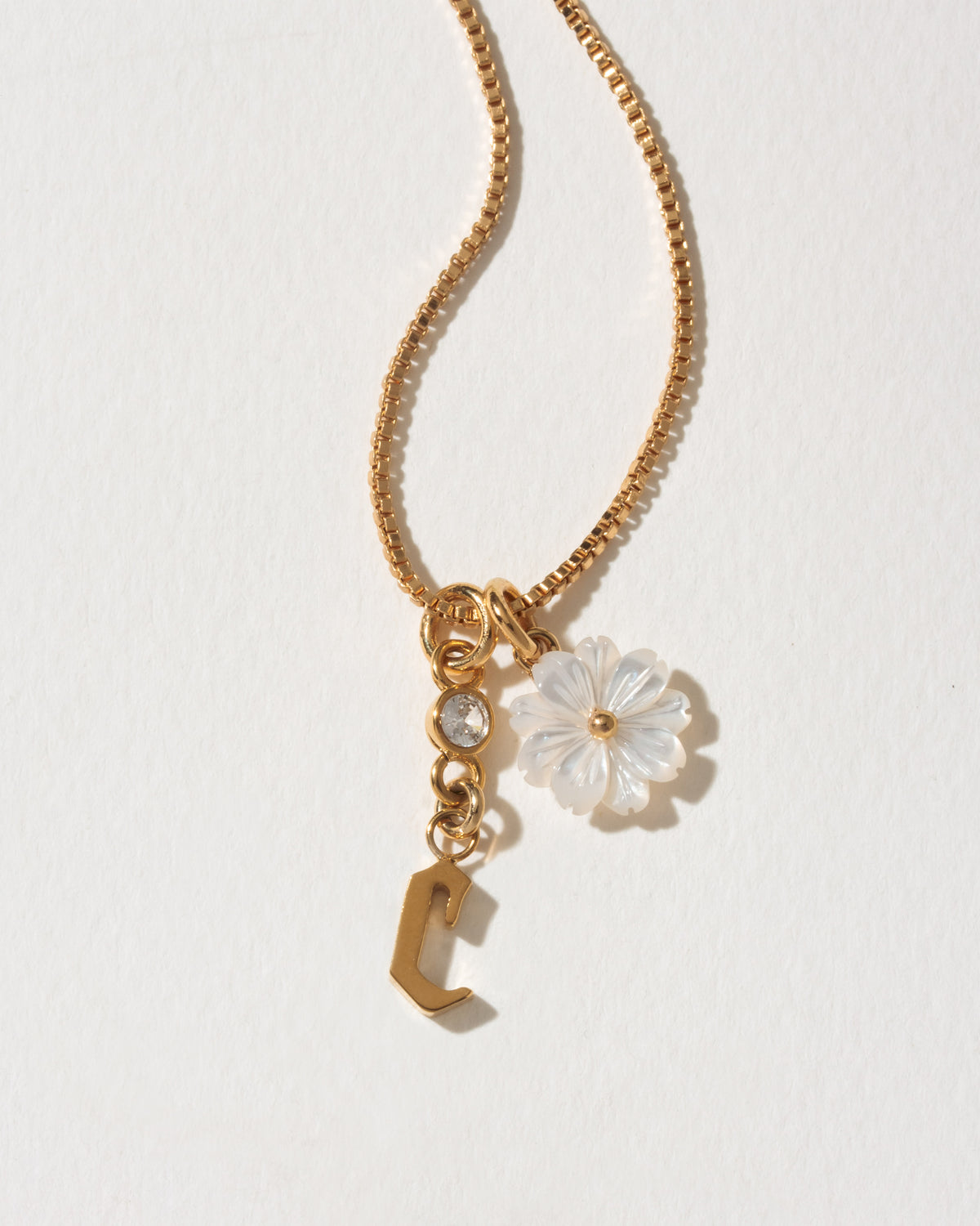 Gold necklace with a letter 'c' and floral pendant on a light background