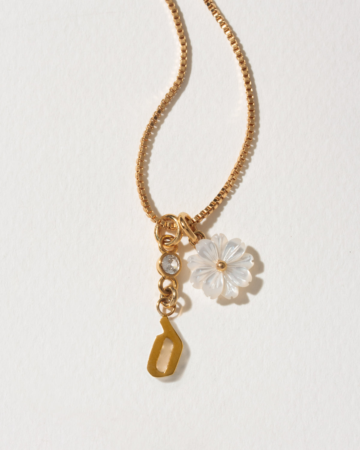 Gold necklace with a letter 'd' and flower charm on a light background