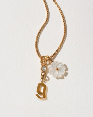 Gold necklace with a flower charm and letter 'g' on a light background