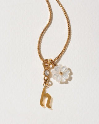 Gold necklace with a flower and letter 'h' charm on a light background