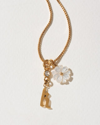 Gold necklace with a flower and letter 'k' charm on a light background