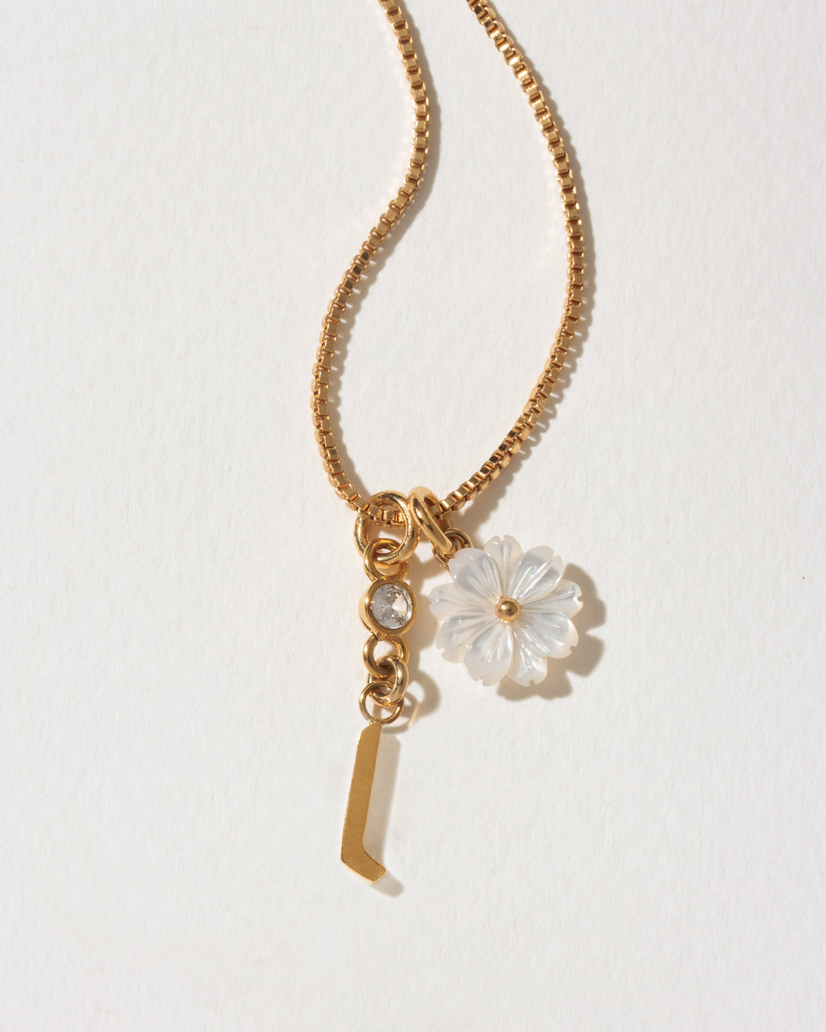 Gold necklace with a flower and letter  'l' charm on a light background