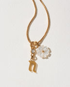 Gold necklace with a flower and letter 'n' pendant on a light background