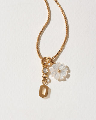 Gold necklace with a letter 'o' and a floral pendant on a light background
