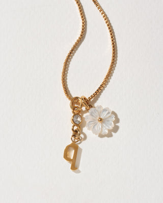 Gold necklace with a flower and letter 'Q' charm on a light background
