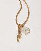Gold necklace with a flower and letter 'r' charm on a light background
