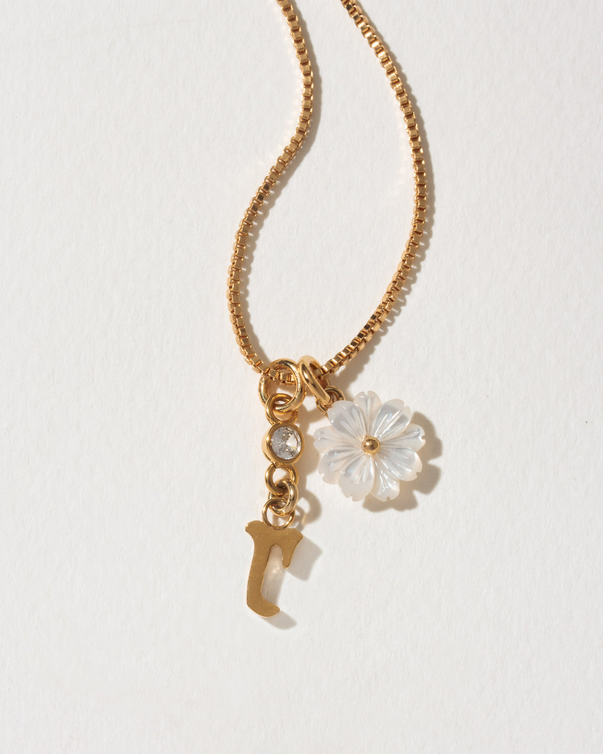 Gold necklace with a flower and letter 'r' charm on a light background