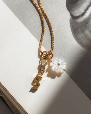 Gold necklace with a letter 's' and a  floral pendant on a light background