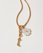 Gold necklace with a flower charm and letter 't' pendant on a light background