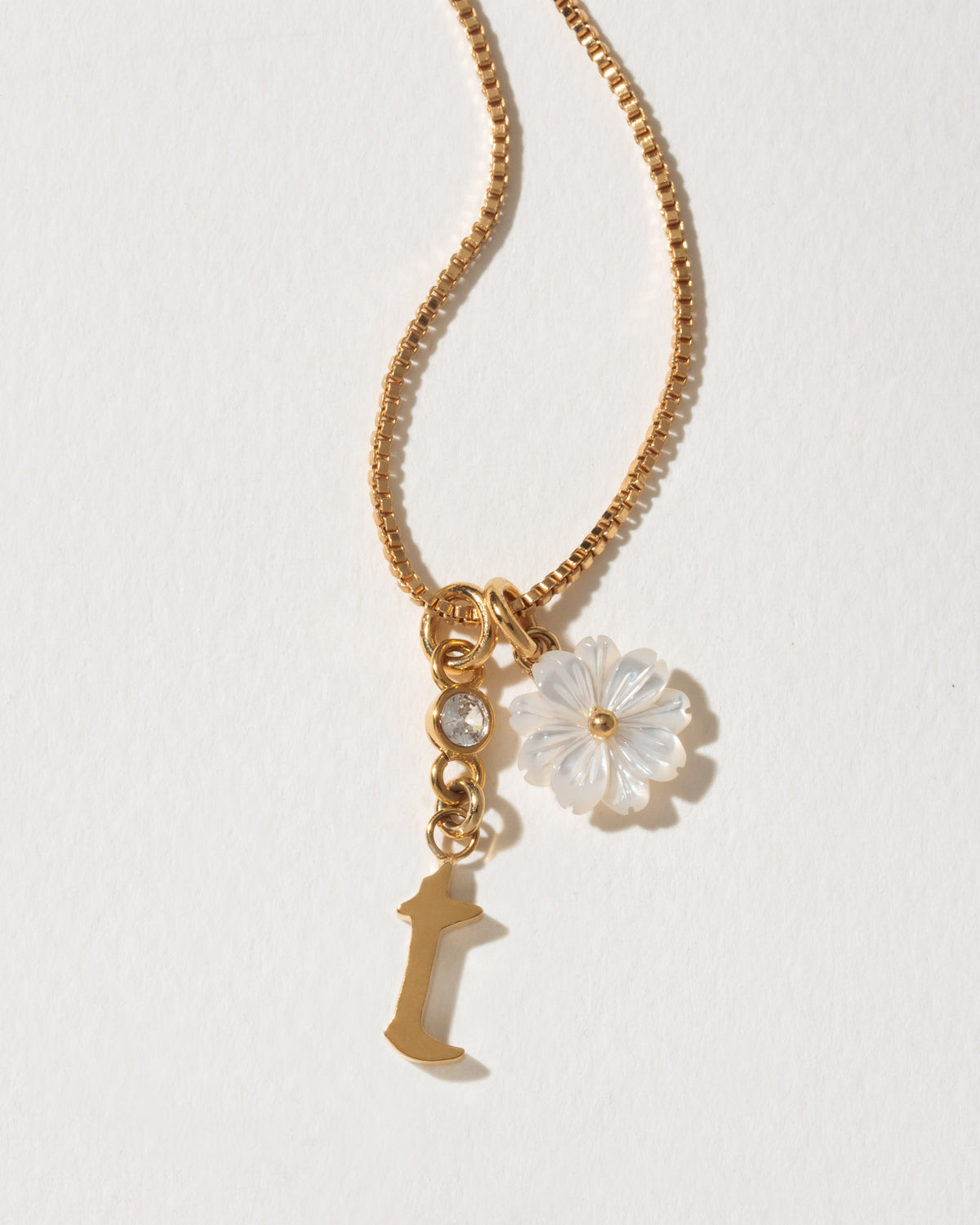 Gold necklace with a flower charm and letter 't' pendant on a light background