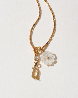 Gold necklace with a flower and letter 'u' charm on a light background