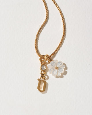Gold necklace with a flower and letter 'v' charm on a light background