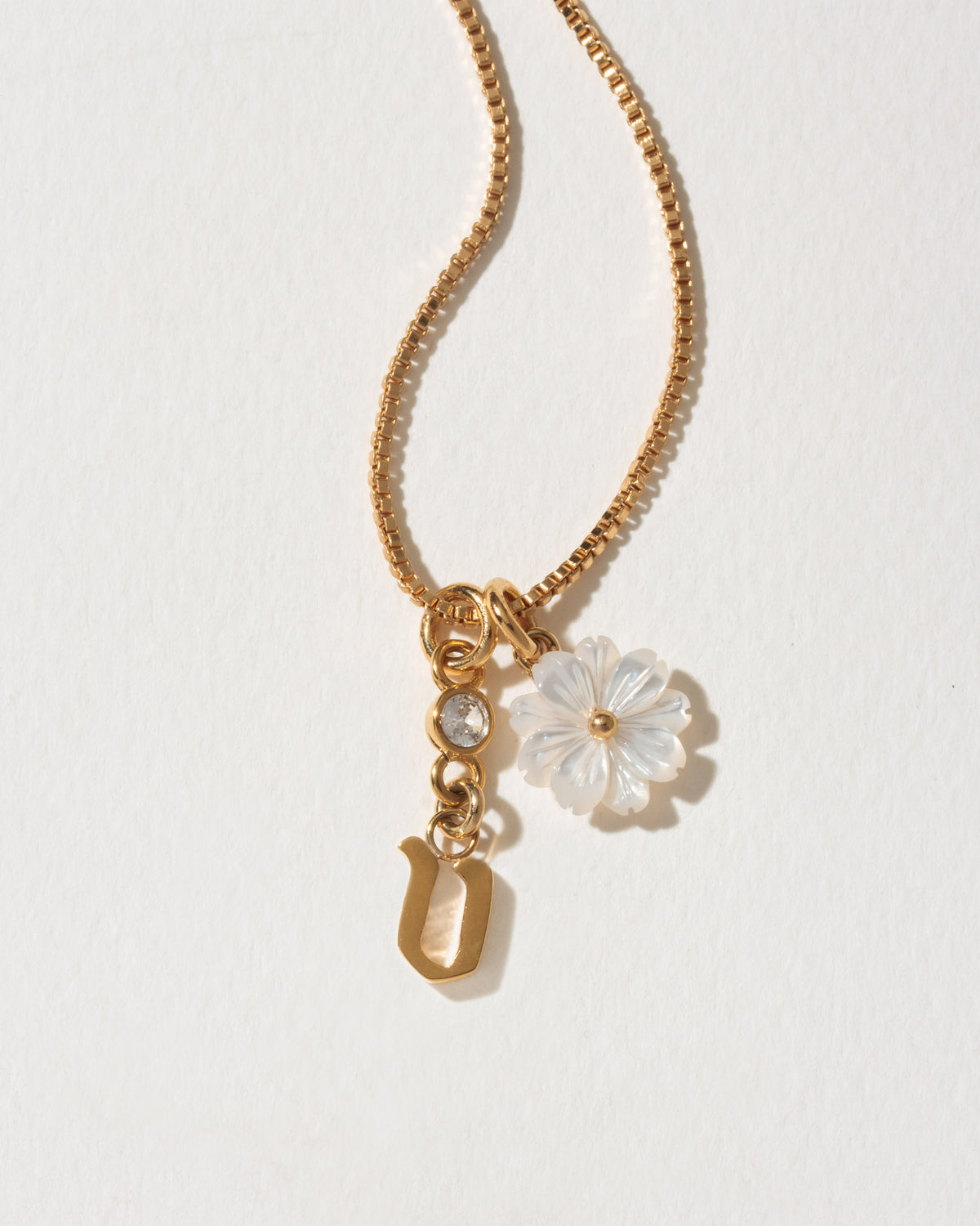 Gold necklace with a flower and letter 'v' charm on a light background