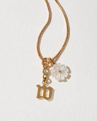 Gold necklace with a floral pendant and letter 'W' charm on a light background